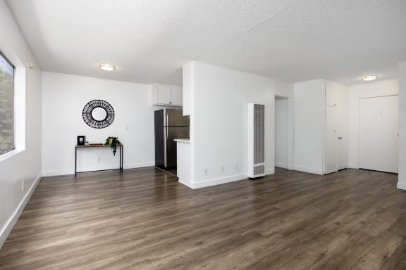 an empty living room and kitchen with white walls and wood flooring