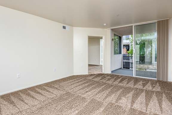 an empty living room with a carpet and a glass door to a hallway