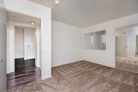 a spacious living room with carpet and a mirrored door to a bedroom
