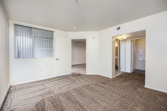 an empty living room with carpet and a door to a bedroom