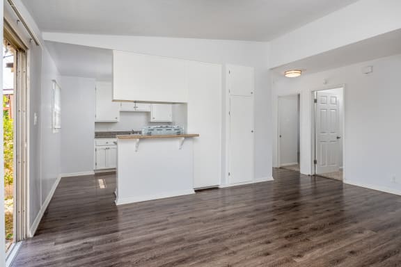 the living room and kitchen of an apartment with white cabinets and a wood floor