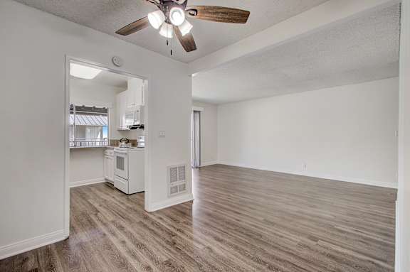 an empty living room with a ceiling fan and a kitchen