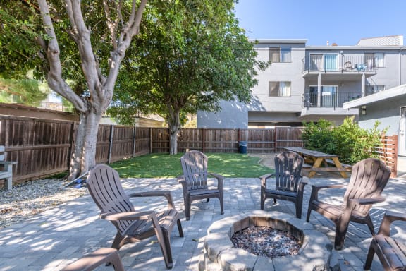 a backyard with a fire pit and chairs and a tree