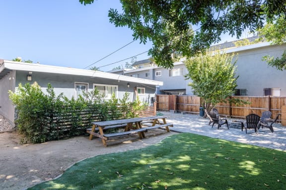 a yard with a picnic table and chairs in front of a house