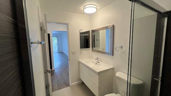 A white bathroom with a sink, mirror, and toilet.