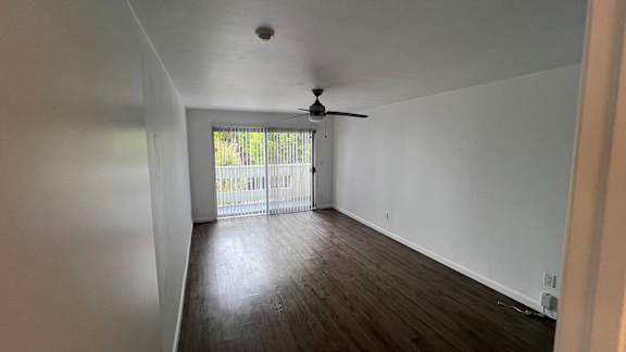 A room with a ceiling fan and sliding glass doors leading to a balcony.