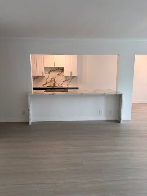 A kitchen island with a marble countertop is in the middle of a room with white walls and wood flooring.