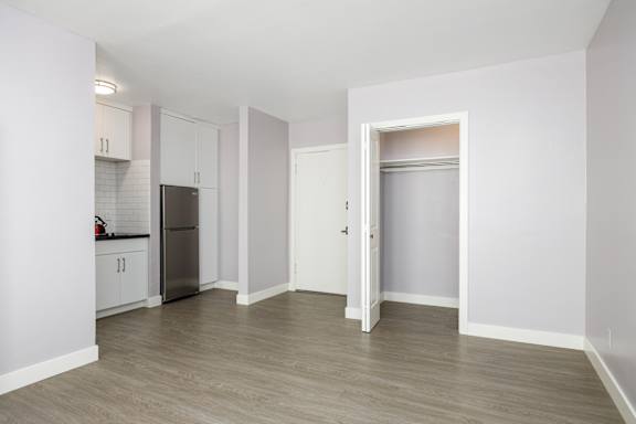 an empty living room with white walls and a stainless steel refrigerator