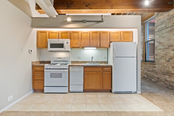 a kitchen with white appliances and wooden cabinets and a brick wall