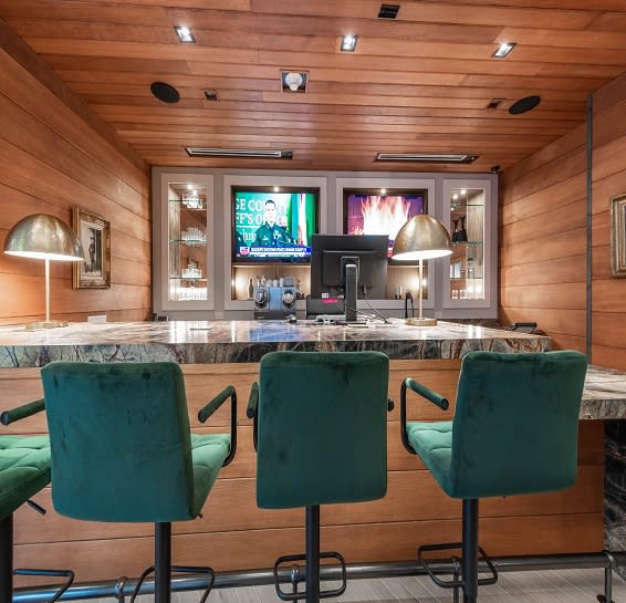 a bar with three green chairs in a room with a television
