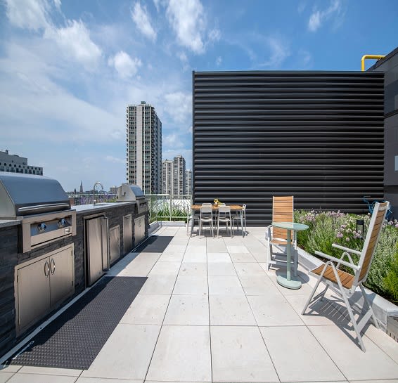 the rooftop patio of a building with a grill and a table and chairs