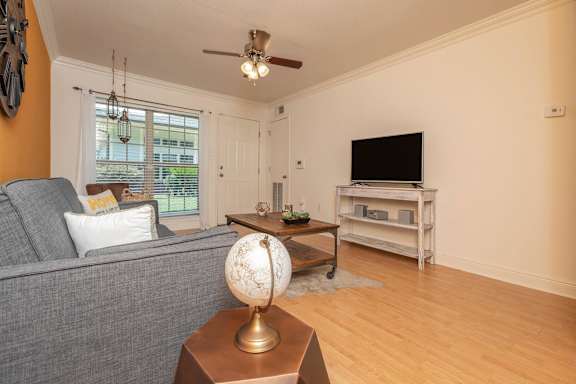 A living room with a grey couch, a wooden coffee table, and a television on a stand. at The Cove at State Street Apartments, Baton Rouge, LA