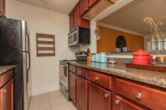 A kitchen with a black fridge, wooden cabinets, and a granite countertop. at The Cove at State Street Apartments, Baton Rouge, Louisiana