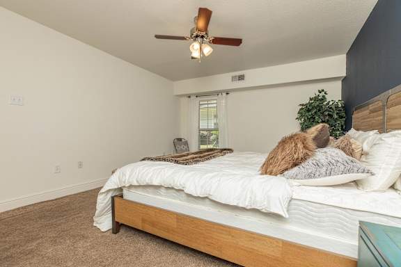 A bedroom with a bed, pillows, a ceiling fan, and a window with blinds. at The Cove at State Street Apartments, Baton Rouge, LA