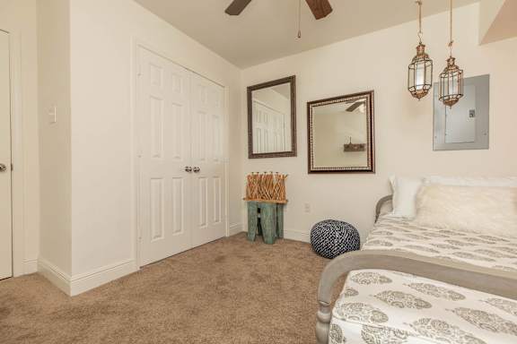 A bedroom with a bed, a mirror, a ceiling fan, and a wall-mounted light fixture. at The Cove at State Street Apartments, Baton Rouge, Louisiana