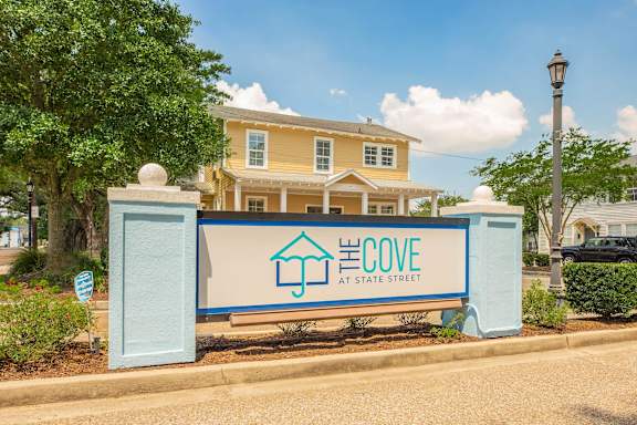 A sign for El Cove at State Street in front of a yellow house. at The Cove at State Street Apartments, Baton Rouge, LA