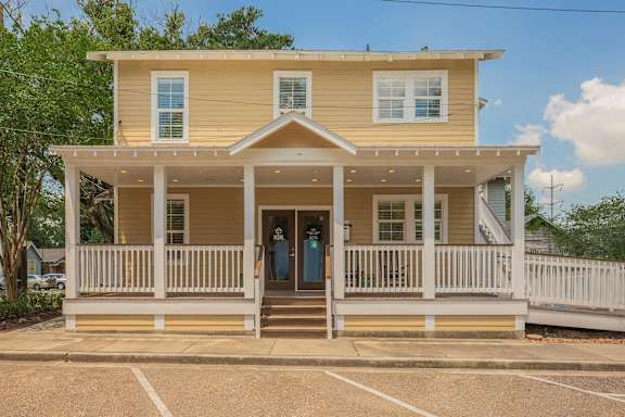 A yellow house with a porch and a white fence. at The Cove at State Street Apartments, Baton Rouge, LA, 70802