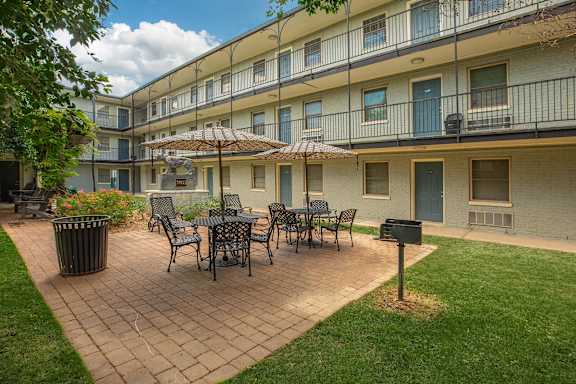 A patio with a table and chairs is surrounded by a grassy area and a building. at The Cove at State Street Apartments, Louisiana