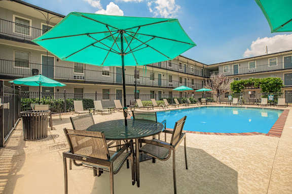 A table with chairs and umbrellas is set up by a pool. at The Cove at State Street Apartments, Louisiana, 70802