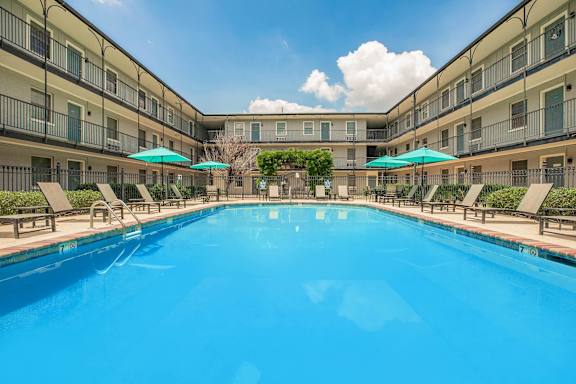 A large swimming pool in a resort with sun loungers and umbrellas. at The Cove at State Street Apartments, Baton Rouge, LA