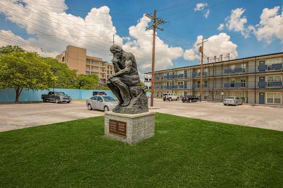 A statue of a man reading is in the middle of a grassy area. at The Cove at State Street Apartments, Baton Rouge, LA