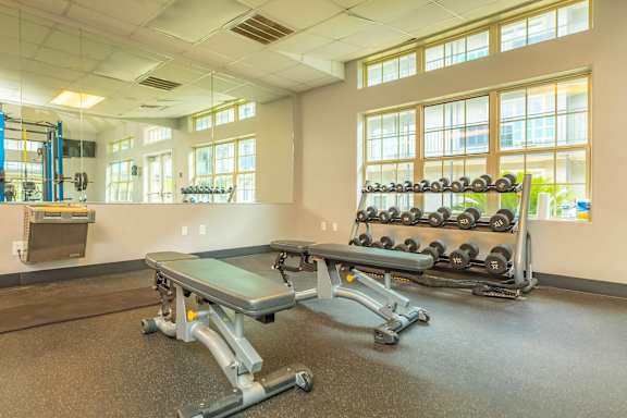 A gym with a bench, weights, and windows. at The Cove at State Street Apartments, Louisiana, 70802