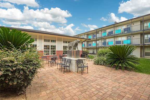 A patio with a table and chairs is surrounded by plants and a brick building. at The Cove at State Street Apartments, Louisiana