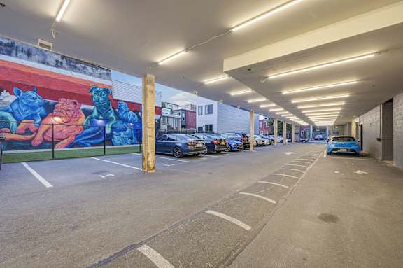 A parking garage with a mural on the wall and cars parked in the spaces.