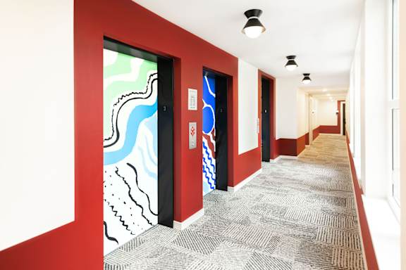 A hallway with a red wall and a carpeted floor.