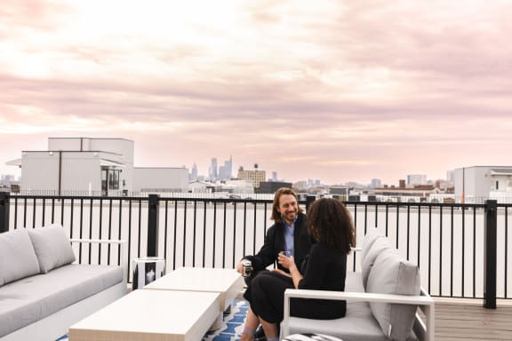 a man and woman sitting on a couch on a roof terrace overlooking the city