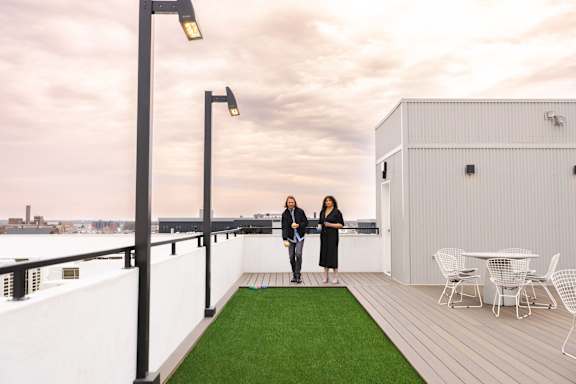 Two people are standing on a balcony with a table and chairs.