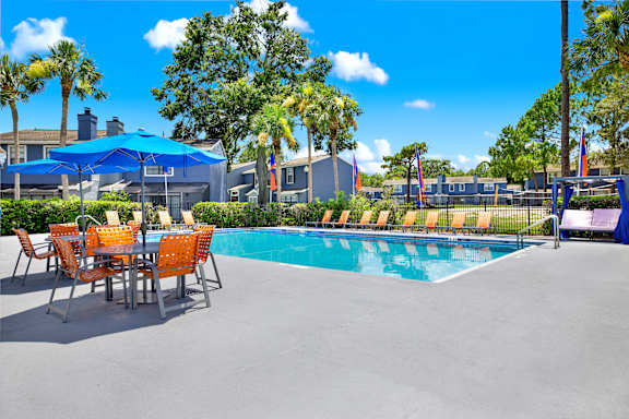 A pool area with a table and chairs and a blue umbrella.