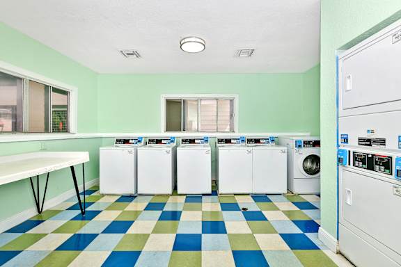 A laundry room with a checkered floor and a row of washers and dryers  at Village Springs in Orlando FL.