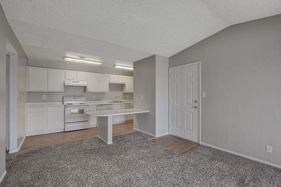 A kitchen with white cabinets and appliances, a dining table, and a carpeted floor.