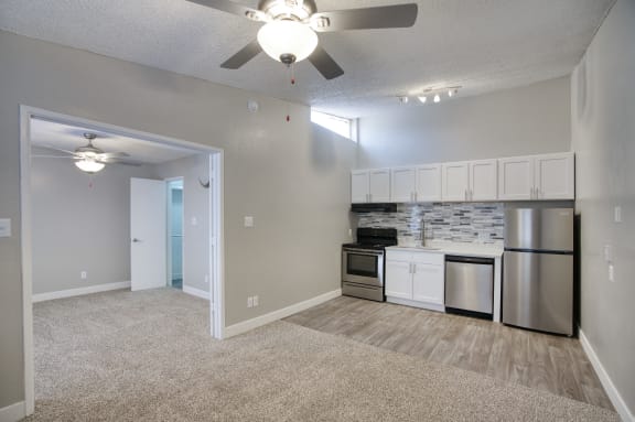 a living room with a ceiling fan and a kitchen with stainless steel appliances