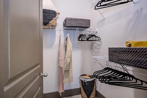 A closet with clothes hanging and a basket on the floor.