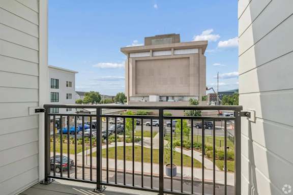 A balcony with a metal railing overlooks a parking lot and buildings.