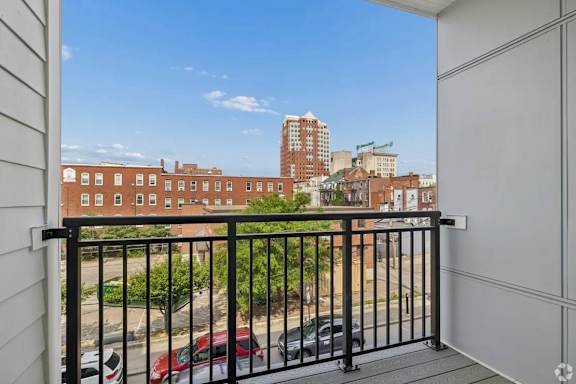 A balcony with a black railing overlooks a parking lot and buildings.
