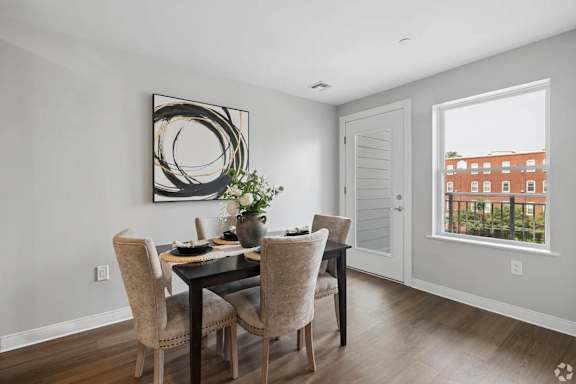 A dining room with a table set for two and a view of a red building outside the window.