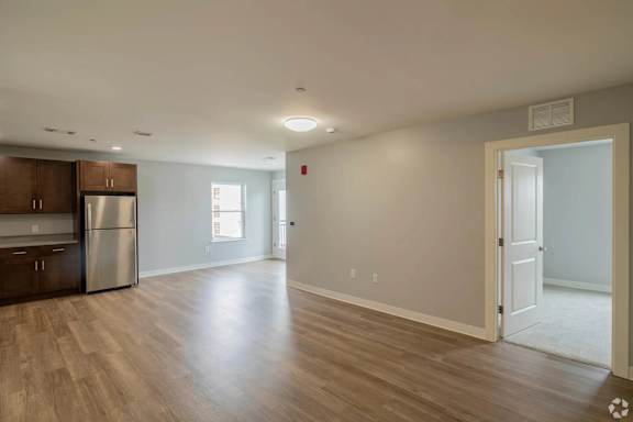 A spacious room with wooden flooring and a kitchen area to the left.