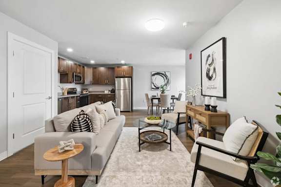 A living room with a grey couch, a wooden coffee table, and a glass table with a plant on it.