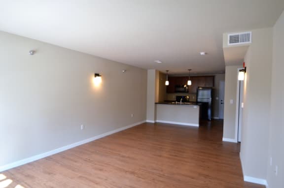 an empty living room with a kitchen in the background