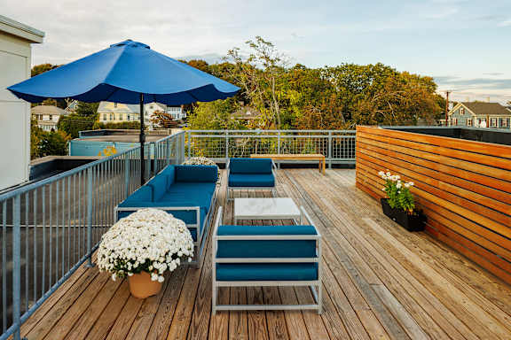 A blue umbrella is on a wooden deck with a white flower pot.
