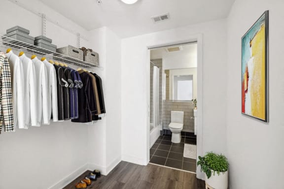 a walk in closet with clothes on a rack and a bathroom with a toilet