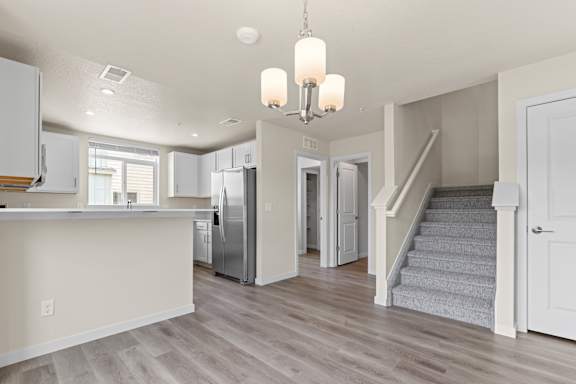 A kitchen with a refrigerator, stairs, and a chandelier.