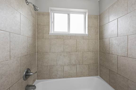 A white bathtub with a shower head and a window above it.