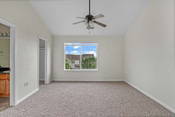 A room with a ceiling fan and a window showing a house outside.