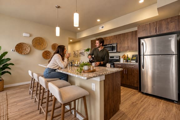 Two people are standing in a kitchen with a refrigerator on the right.