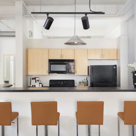 A kitchen with a black fridge and microwave, a black countertop, and brown chairs.