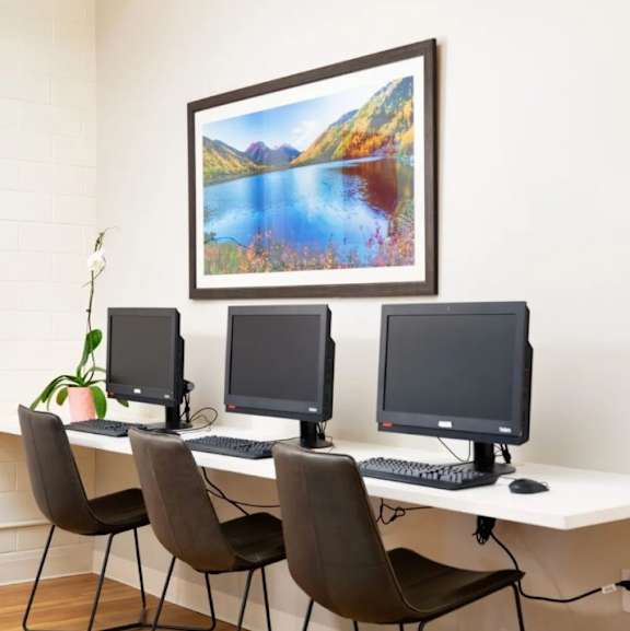 Three monitors are on a desk with a picture of a lake above them.